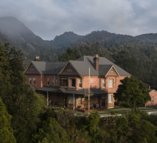 An imposing brick building with peaked grey roof surrounded by trees and wispy clouds due to the elevation