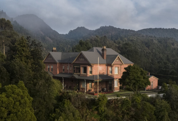 An imposing brick building with peaked grey roof surrounded by trees and wispy clouds due to the elevation