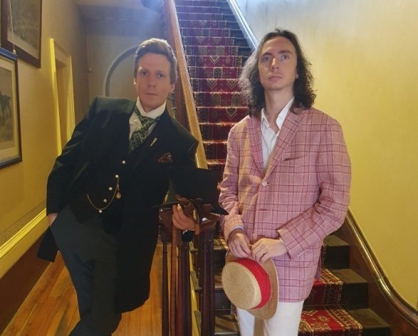 Two men post strikingly infront of a grand staircase while dressed in period costume