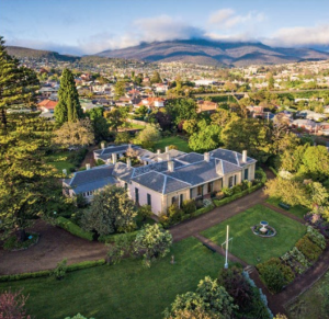 A wide image of Runnymede house, a sprawling single story home amongst lush heritage gardens. Mount Wellington can be seen in the background.