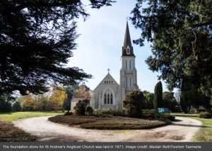 Surrounded by trees is a tall white church with a tall steeple and grey roof.