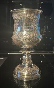 A heavily engraved silver cup on a dark background