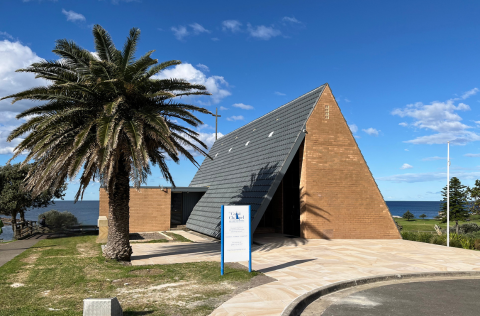 An A-frame 20th century building in the foreground with the sea in the background.
